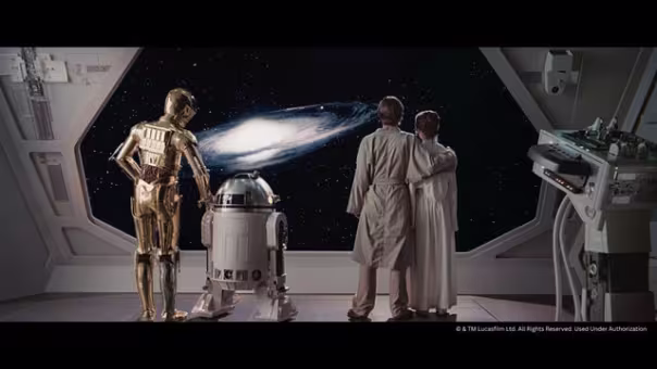 A scened from Star Wars where Luke and Leah wear white robes and look out of the window of a grey space ship at a galaxy with C3PO a golden humanoid robot and R2D2 a waist-high, blue and white robot with a cylindrical body, dome head, and a pair of sturdy legs that descend from its shoulder area.