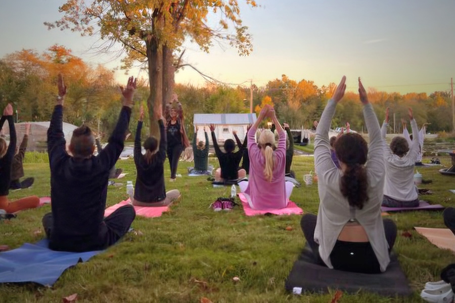 A group raises hands in the air while sitting on yoga mats on the ground