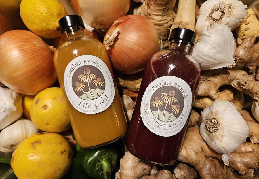 two bottle s of fire cider sat among fruits and vegetables