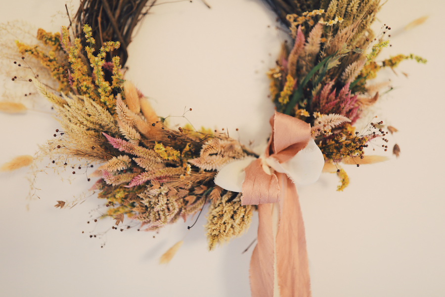 wreath of sticks and dried flowers and grasses in fall colors with a pink bow